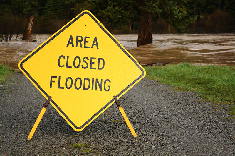 Yellow sign saying Area Closed Flooding in front of flooded road.
