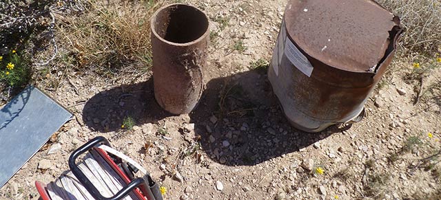 Image of a metal well head in a rocky landscape with a water level measuring tape in the lower left corner